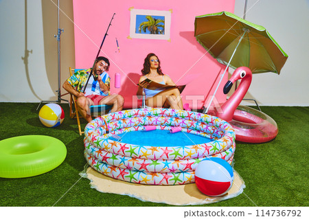 Couple creates beach party sitting, sunbathing and relaxing by inflatable kiddie pool and toasting with drinks. Pop art style. Couple creates beach party sitting, sunbathing and relaxing by inflatable kiddie pool and toasting with drinks. Pop art style. 114736792