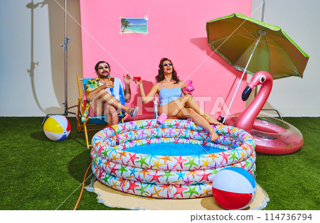 Cheerful couple, man and woman in retro attire, relaxes by a kiddie pool they toast to summer fun sitting relaxes by kiddie pool 114736794