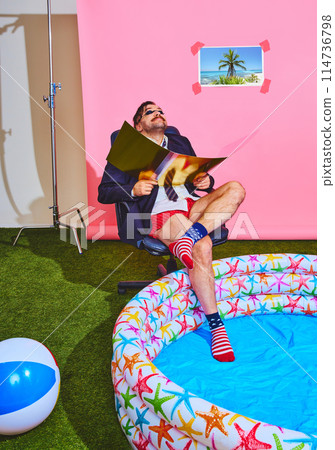 Man in business attire and swim shorts enjoys a makeshift vacation in office in kids pool. Retro colors. Remote work. 114736798