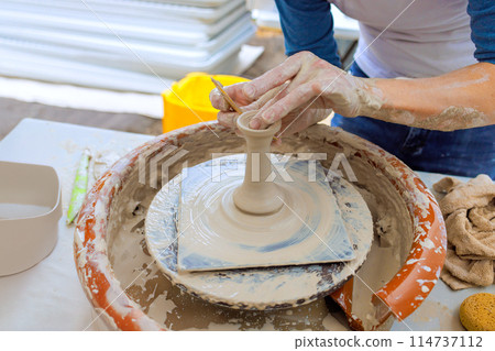 In potter is sculpting soft clay with wet hands while making clay dishes on potter wheel 114737112