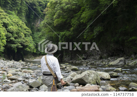 A man fishing in a mountain stream in early summer A man fishing in a mountain stream in early summer 114737758