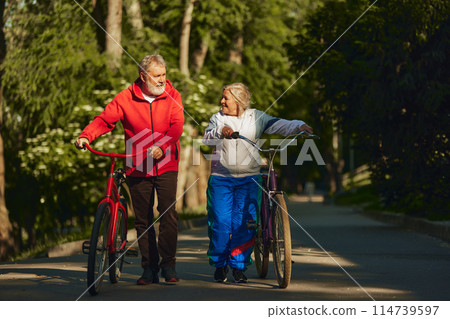 Senior couple, smiling, happy man and woman, joyfully bicycles through park, showing enduring spirit and love for outdoor activities Senior couple, smiling, happy man and woman, joyfully bicycles through park, showing enduring spirit and love for outdoor activities 114739597