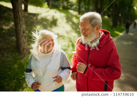 Morning Active Routine. Happy and energetic couple, elderly man and woman going on morning jogging activity in the park on sunny day. 114739610