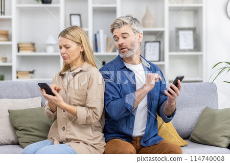 Couple sitting on couch looking upset while using smartphones, highlighting relationship issues and technology's impact on communication. 114740008
