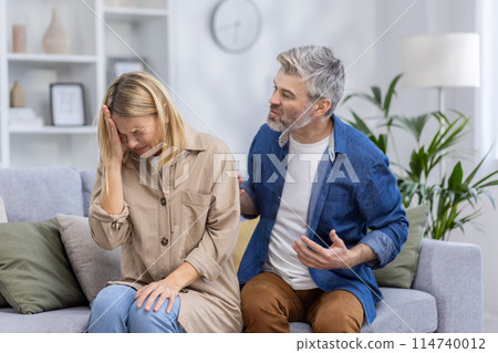 A middle-aged couple is seen arguing in their living room, depicting emotions of frustration and sadness in a domestic environment. 114740012