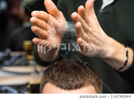 A barber deftly styles a clients hair with powder in the barbershop. 114740044