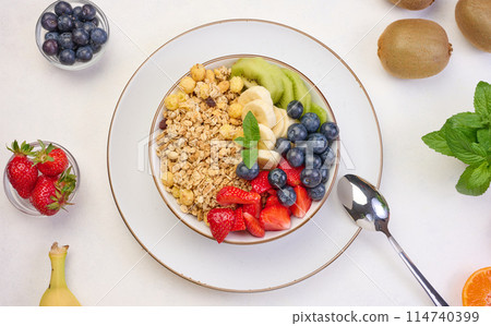 Granola with strawberries, kiwi, banana and blueberries in a round plate on a white table. Granola with strawberries, kiwi, banana and blueberries in a round plate on a white table. 114740399