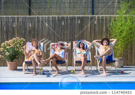 Group of cheerful seniors lying on lounge chairs by swimming pool and sunbathing. Spending hot day outdoors in backyard. Group of cheerful seniors lying on lounge chairs by swimming pool and sunbathing. Spending hot day outdoors in backyard. 114740483