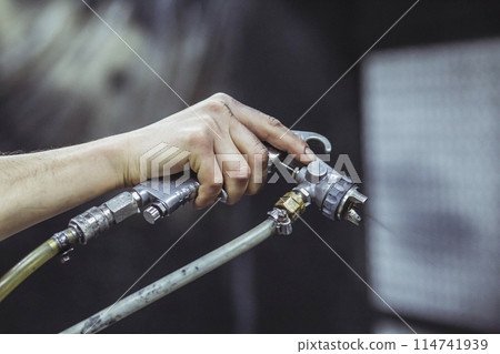 A worker paints with a spray gun at a factory. Close-up A worker paints with a spray gun at a factory. Close-up 114741939