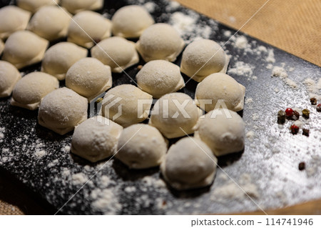 Traditional russian pelmeni, ravioli, dumplings with meat on black wood background. Top view. Copy space Traditional russian pelmeni, ravioli, dumplings with meat on black wood background. Top view. Copy space 114741946