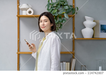 一位年輕女子在房間裡看著她的智慧型手機 一位年輕女子在房間裡看著她的智慧型手機 114742807