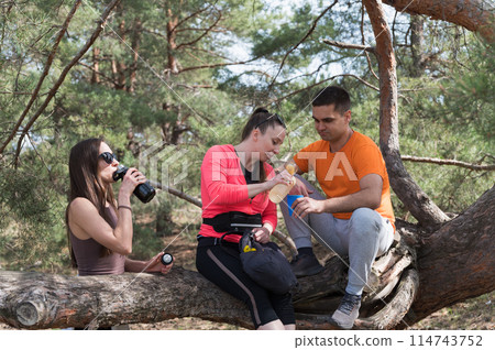 Three friends rest on a fallen log during a hike. 114743752