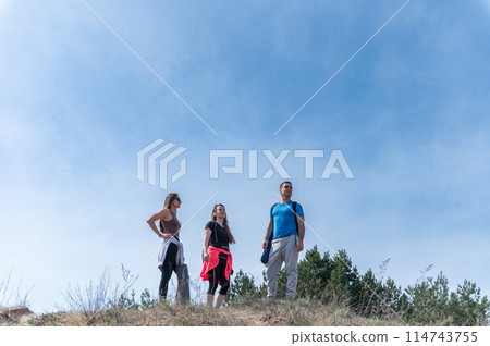 Three friends in sportswear stand on a hill against the sky. Three friends in sportswear stand on a hill against the sky. 114743755