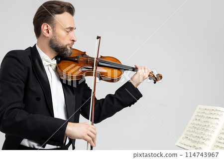 Man violinist with beard playing violin while facing sheet of music Man violinist with beard playing violin while facing sheet of music 114743967