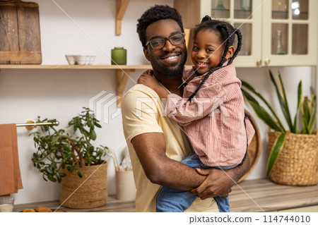 Smiling black man holding his little daughter in kitchen interior 114744010