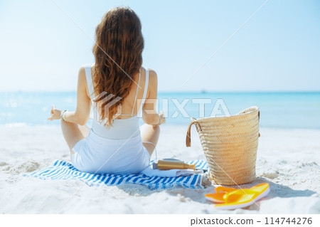 Seen from behind woman on seashore listening to music 114744276