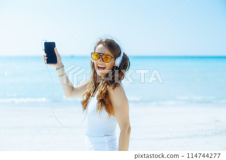 happy female on seacoast dancing and listening to music 114744277