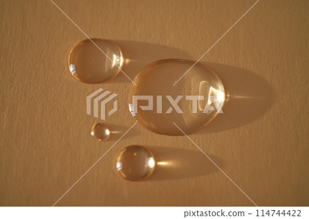 Beautiful volumetric drops of cosmetic product on a beige background. Beautiful volumetric drops of cosmetic product on a beige background. 114744422