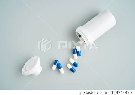Blue and white capsules spilled out of a medicine jar on a blue background. 114744450
