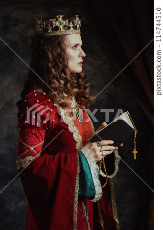 medieval queen in red dress with book, rosary and crown 114744510