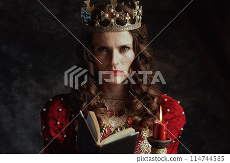 medieval queen in red dress with book, candle and crown medieval queen in red dress with book, candle and crown 114744585