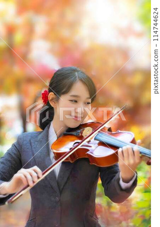 A woman playing the violin against a background of autumn leaves 114744624