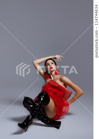 A young girl in a red dress in the studio posing on a white background. 114744634