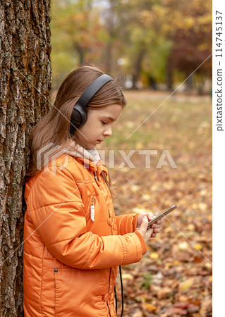 A girl listens to music on headphones in an autumn park 114745137