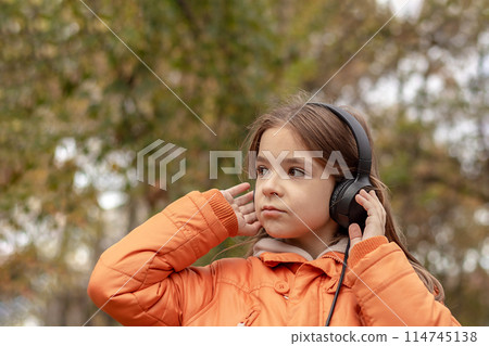 A girl listens to music on headphones in an autumn park. Copy space 114745138