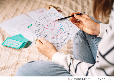 Tarot reader reads natal chart with tarot cards while sitting on bed 114745249