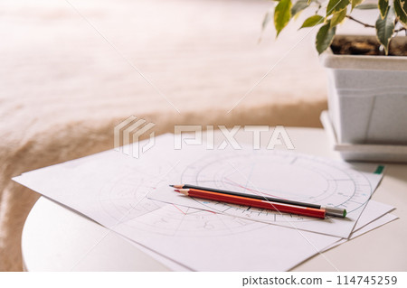 Natal chart on white paper with pencils on a table with a flower opposite the bed 114745259