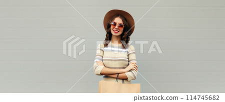 Stylish beautiful happy smiling young woman posing with shopping bags in round hat, gray background Stylish beautiful happy smiling young woman posing with shopping bags in round hat, gray background 114745682
