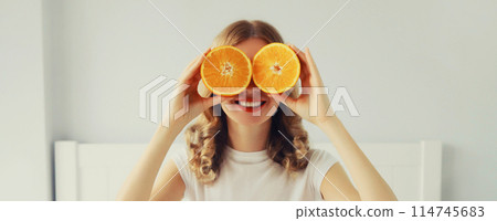 Happy healthy cheerful young woman covering her eyes with slices of orange fruits and looking for 114745683