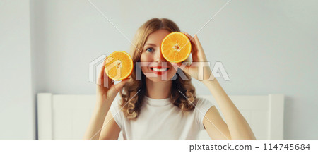 Happy healthy cheerful young woman with slices of orange fruits in white room at home 114745684