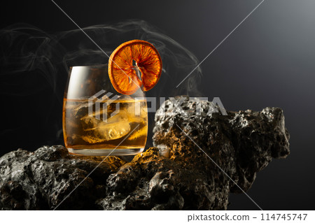 Smoked old fashioned cocktail with ice and dried orange slice. 114745747