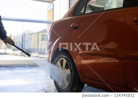 Directing a stream of water at a car wheel, a man washes dirt from the rims. The man holds a pistol in his hands and washes away dirt from his car with a stream of water. The concept is my self. 114745832