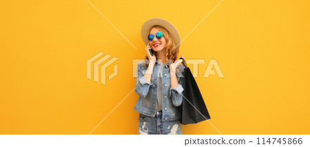 Beautiful young woman calling on smartphone with black shopping bag, summer hat on yellow background 114745866
