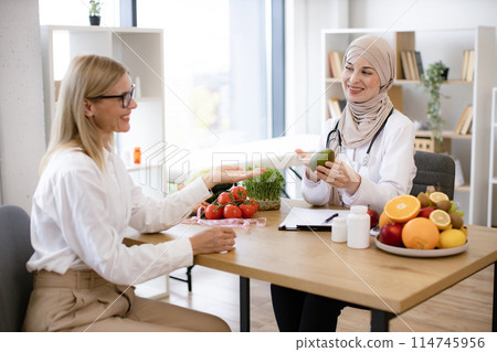 Nutritionist talks to patient about benefits of healthy diet holding avocado. Nutritionist talks to patient about benefits of healthy diet holding avocado. 114745956