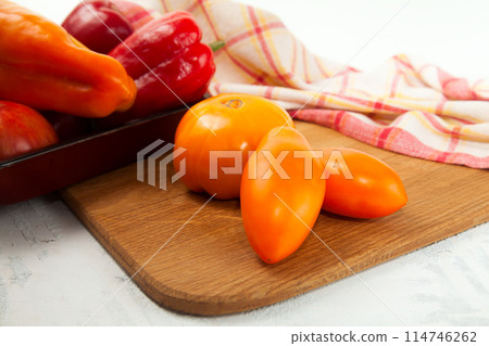 Cutting board with assort of different tomatoes and bell pepper on white wooden background.. 114746262