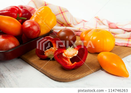Cutting board with assort of different tomatoes and bell pepper on white wooden background.. 114746263