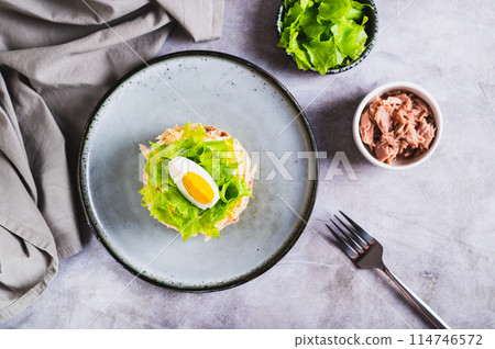 Appetizing salad of canned tuna, potatoes, cheese, lettuce and eggs on a plate top view 114746572