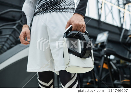 Close up of unrecognizable man holding VR headset in hand with exercise machines in background copy space Close up of unrecognizable man holding VR headset in hand with exercise machines in background copy space 114746697