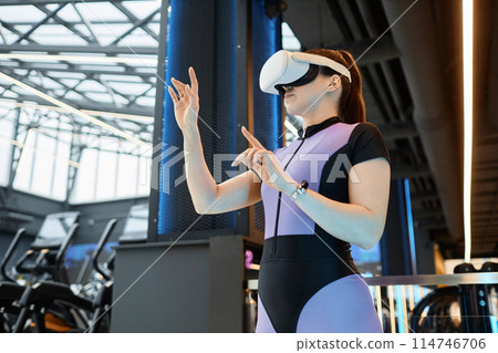 Side view portrait of young sportswoman wearing VR headset in futuristic gym training and using interactive hand tracking copy space 114746706