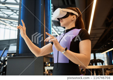Side view portrait of young sportswoman wearing VR headset in gym and using interactive technology copy space Side view portrait of young sportswoman wearing VR headset in gym and using interactive technology copy space 114746708