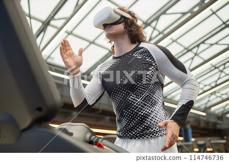 Action side view of muscular young man running on treadmill with VR headset in futuristic gym copy space 114746736