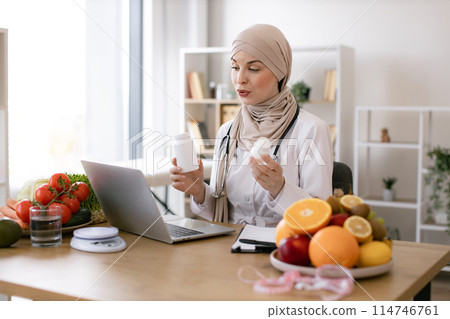 Positive arabian nutritionist woman holding pills or vitamins in hands. Positive arabian nutritionist woman holding pills or vitamins in hands. 114746761