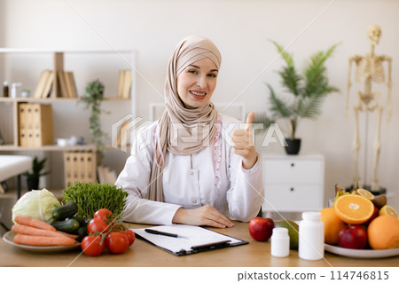 Smiling young dietician sitting at desk Smiling young dietician sitting at desk 114746815