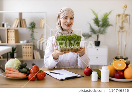 Lady in white coat holding container with microgreens while sitting at desk. 114746826