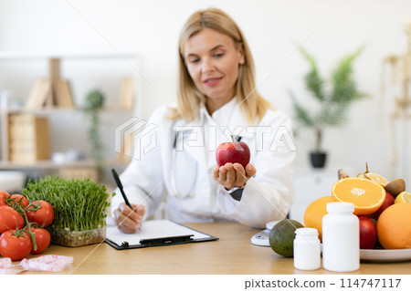 Portrait of female posing with apple while doing paperwork in doctor's office. Portrait of female posing with apple while doing paperwork in doctor's office. 114747117