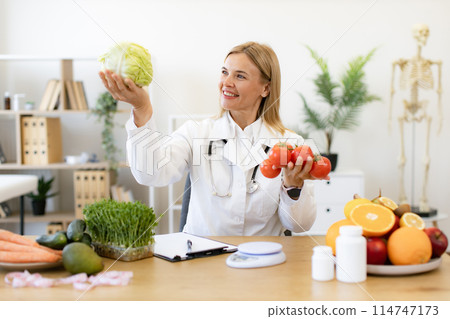 Mature female doctor nutritionist holds fresh organic tomatoes and cabbage. 114747173